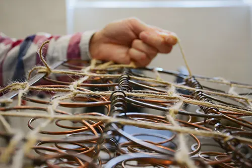 Polsterspringfedern. Polsterer beim Binden alter Federn. Polsterwerkstatt. Restaurierung alter Stuhlspringfedern. Frau bei der Arbeit. Hand und Schnur.