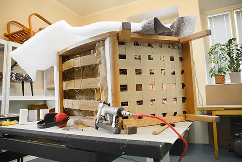 Innenansicht einer Polsterei. Renovierung eines alten Stuhls aus den 50er Jahren. Polsterwerkzeuge auf dem Tisch. Reparatur alter Möbel. Holzkonstruktion mit Federn und Gurten.